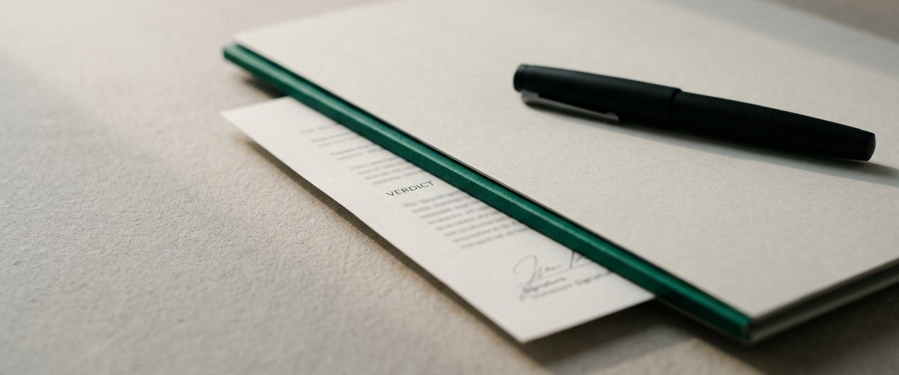A document folder with an emerald edge band and a fountain pen resting on top in low evening light